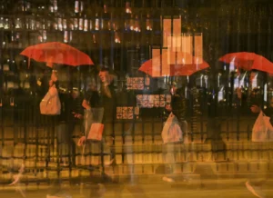 Pierre · 20/12/2025 · 4426 x 3217 Cette photographie capture une scène nocturne urbaine sous la pluie. Le sujet principal est un groupe de personnes protégées par des parapluies rouges, marchant ou stationnant près d’un grillage métallique.La composition met en avant les lignes verticales des parapluies et des barrières, créant un effet graphique. Le cadrage serré isole les personnages, les rendant flous et anonymes. La lumière est tamisée, avec des éclairages artificiels jaunâtres en arrière-plan, donnant une ambiance nocturne et mystérieuse. Les couleurs dominantes sont les rouges vifs des parapluies et les tons froids et sombres de la nuit. Le style est réaliste et légèrement flou, renforçant l’atmosphère humide et dynamique de la ville la nuit.