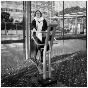 Marc Lavorata · 06/12/2025 · 1100 x 1100 Cette photographie en noir et blanc met en scène une femme comme sujet principal, assise sur un appareil de musculation en extérieur. La composition est simple et centrée, avec un cadrage serré sur le sujet et son environnement immédiat.La lumière semble naturelle, probablement en journée, éclairant le sujet de manière uniforme. Les ombres sont peu marquées, suggérant un temps nuageux ou une lumière douce.L’ambiance est calme et fonctionnelle, renforcée par les tons de gris et les contrastes subtils. Le style est documentaire et sobre, capturant un moment de quotidienneté.