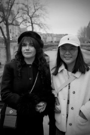 Thomas · 13/12/2025 · 2048 x 3080 Cette photographie en noir et blanc met en scène deux femmes comme sujets principaux, posant côte à côte. La composition est simple et symétrique, avec un cadrage serré sur elles. La lumière semble naturelle, douce mais contrastée, mettant en valeur leurs visages.Les couleurs dominantes, bien que réduites au noir et blanc, suggèrent des tons sombres (vêtements épais) et clairs (visages, accessoires). Le style est sobre et documentaire, évoquant une ambiance authentique et intime, probablement urbaine et hivernale.