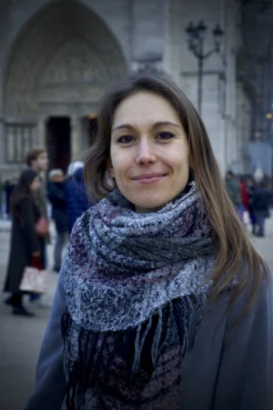 Thomas · 13/12/2025 · 2048 x 3080 Cette photographie met en scène une jeune femme comme sujet principal, souriante, vêtue d’un manteau sombre et d’un large châle à motifs gris et blancs. Le cadrage est serré sur elle, avec un arrière-plan flou montrant une architecture classique et des passants.La lumière semble naturelle, douce et légèrement tamisée, créant des contrastes doux. Les couleurs dominantes sont les tons gris, blancs et quelques touches de brun et beige. Le style est simple et spontané, évoquant une ambiance chaleureuse et urbaine, probablement en ville. L'atmosphère est conviviale et authentique.