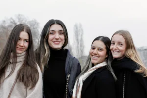 Cédric · 13/12/2025 · 5184 x 3456 Cette photographie met en scène quatre jeunes femmes souriantes, formant le sujet principal. La composition est symétrique et serrée, avec un cadrage rapproché sur leurs visages.La lumière est douce et naturelle, probablement en extérieur par temps nuageux, créant une ambiance lumineuse mais sans ombres marquées. Les couleurs dominantes sont les tons froids et neutres : gris, noir et blanc, adoucis par les teintes chaudes des vêtements (beige, marron).Le style est épuré et spontané, évoquant une ambiance chaleureuse et amicale.