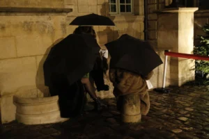 Cédric · 20/12/2025 · 5184 x 3456 Cette photographie montre deux statues ou mannequins habillés en personnages historiques, penchés vers des bassins. Le sujet principal est cette scène de rue nocturne, évoquant une activité artisanale ou théâtrale.La composition est symétrique, avec un cadrage serré centré sur les personnages. L’éclairage est tamisé, créant une ambiance mystérieuse et dramatique. Les couleurs dominantes sont les teintes sombres (noirs, gris) avec des touches de beige et de rouge (le tapis).Le style rappelle une mise en scène historique ou une performance artistique, renforçant une atmosphère à la fois réaliste et onirique.
