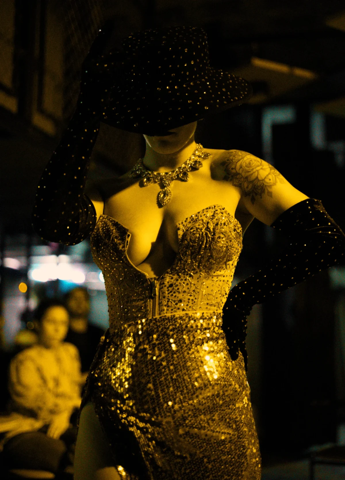 Olivier · 04/10/2025 · 3669 x 5093 Cette photographie met en scène une femme vêtue d’une robe dorée et scintillante, style glamour et élégant. Elle semble danser ou poser sous une lumière tamisée, avec des paillettes tombant autour d’elle, ajoutant un effet magique.Le cadrage est serré sur elle, avec un arrière-plan flou où l’on devine des silhouettes et une ambiance nocturne. Les couleurs dominantes sont le doré éclatant et les tons chauds, créant une ambiance sophistiquée et festive. L’éclairage dramatique accentue le côté mystérieux et sensuel de la scène.
