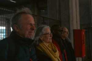 Don · 6664 x 4443 Cette photographie montre quatre personnes âgées observant quelque chose à travers des barreaux, probablement une cage ou une vitrine. Le cadrage est serré sur leurs visages, créant une ambiance intime. La lumière est douce et naturelle, éclairant légèrement leurs traits.Les couleurs dominantes sont sobres : tons gris, bleus et jaunes (notamment le châle de la femme au centre). Le style est documentaire, réaliste, sans retouche apparente. L’ambiance est calme et contemplative, évoquant une scène de visite ou d’observation attentive.