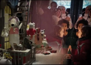Cette photographie semble provenir d’une scène de film ou de théâtre. Le sujet principal est un personnage en costume de style médiéval ou fantastique, entouré de poupées et d’animaux en peluche.La composition est dynamique, avec un cadrage serré sur les éléments proches et un arrière-plan flou. La lumière est douce et légèrement rosée, créant une ambiance mystérieuse et onirique. Les couleurs dominantes sont les tons chauds (rouges, bruns) et des touches de blanc et noir.Le style évoque un mélange de réalisme et de fantastique, renforçant une ambiance à la fois magique et nostalgique.