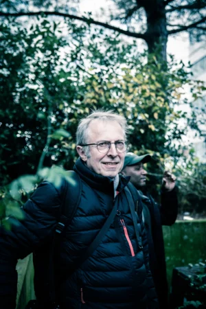 Tery · 4480 x 6720 Cette photographie montre un homme âgé comme sujet principal, souriant et portant une veste de randonnée. Le cadrage est serré, mettant en valeur son visage et sa posture détendue.La composition est naturelle, avec un arrière-plan boisé légèrement flou. La lumière semble douce et naturelle, probablement en extérieur par temps nuageux. Les couleurs dominantes sont les tons verts de la végétation et les teintes neutres de ses vêtements, avec des touches de bleu et rouge.Le style est simple et spontané, évoquant une ambiance chaleureuse et apaisante, typique d’un moment de détente en pleine nature.