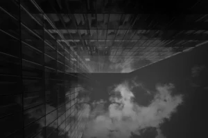 Cette photographie présente un **sujet architectural abstrait**, probablement une structure urbaine vue de bas en haut. La **composition** joue sur les lignes verticales et horizontales, créant un effet de profondeur et de perspective.Le **cadrage** est serré, mettant en valeur les jeux d’ombres et de transparence. La **lumière**, tamisée et contrastée, accentue les contours et les reflets, donnant une impression de nuit ou de faible éclairage.Les **couleurs dominantes** sont des tons de gris et de noir, renforçant une ambiance **sombre et mystérieuse**. Le style, **minimaliste et épuré**, évoque une esthétique moderne et presque onirique. L’ambiance est **suspenseuse et contemplative**.