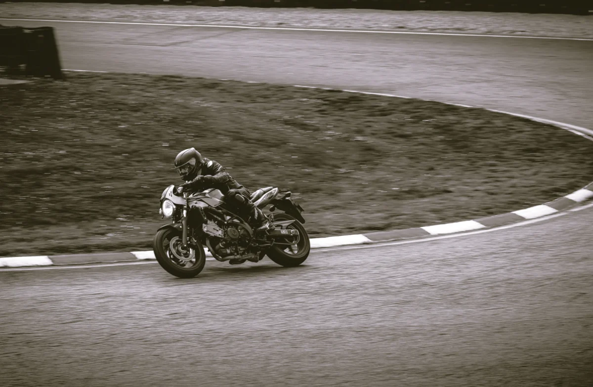 Laurent · 3312 x 2160 Cette photographie met en scène un motocycliste en action sur une piste circulaire. Le sujet principal est le rider, vêtu d’une combinaison intégrale, penché sur sa moto lors d’un virage.La composition est dynamique, centrée sur le mouvement. Le cadrage serré isole le sujet, accentuant l’action. La lumière, naturelle et tamisée, crée des contrastes doux, typiques d’un style noir et blanc.Les tons dominants varient du gris clair au foncé, renforçant l’ambiance sportive et intense. Le style, sobre et cinétique, évoque l’adrenaline et la précision. L’atmosphère est à la fois technique et esthétique, captant l’essence de la vitesse.