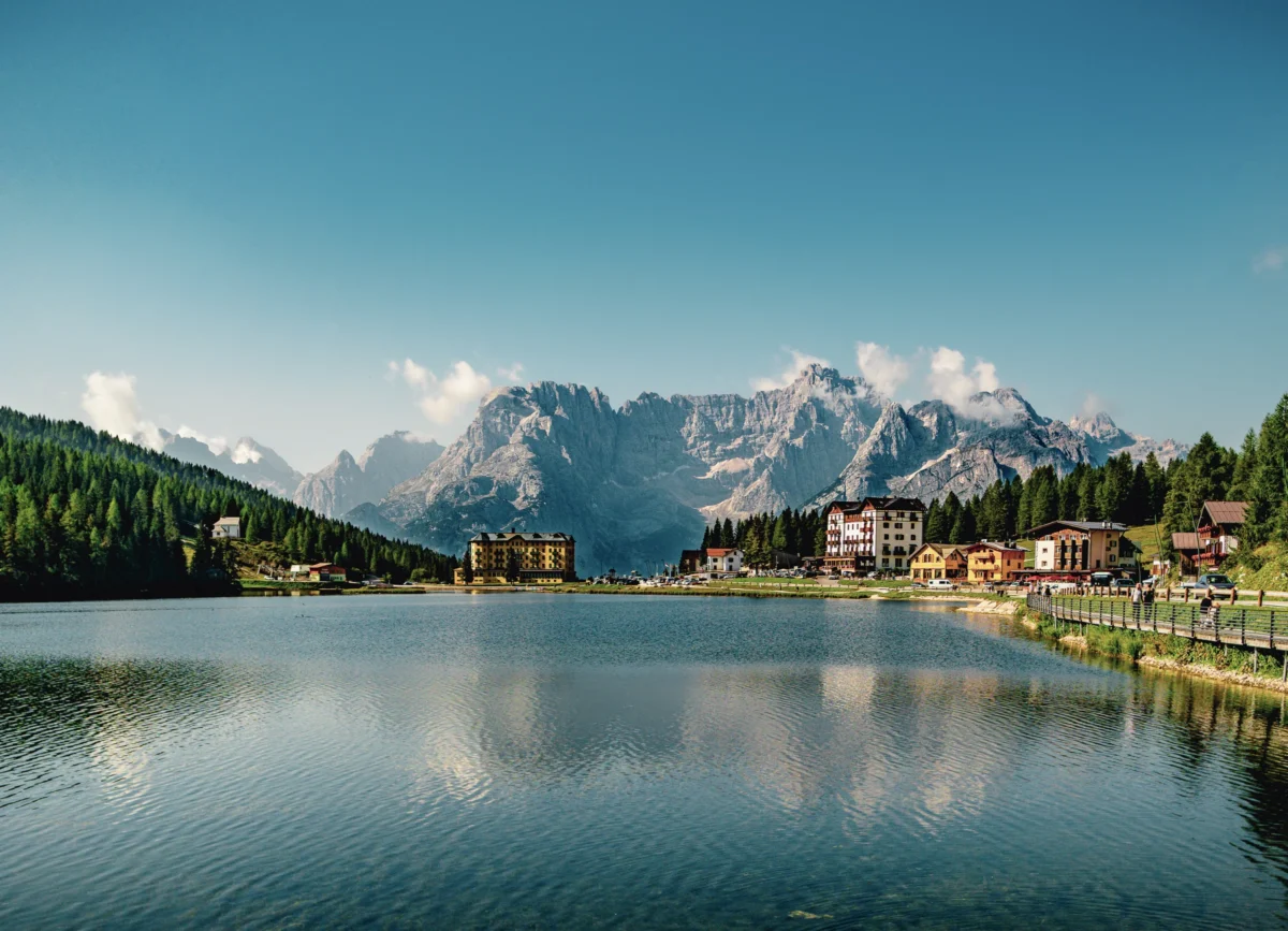 Laurent · 2991 x 2160 Cette photographie met en scène un **lac de montagne** comme sujet principal, reflétant des sommets enneigés et des bâtiments colorés. La **composition** est équilibrée, avec une ligne d’horizon centrale et des éléments architecturaux alignés le long de la rive.Le **cadrage** est large, offrant une vue panoramique. La **lumière** est naturelle et douce, créant des contrastes entre ombres et éclats lumineux. Les **couleurs dominantes** sont les bleus (lac, ciel) et les verts (végétation), rehaussés par des touches de blanc (neige) et de rouge/orange (toits).Le style est **réaliste et apaisant**, évoquant une **ambiance sereine et touristique**, typique des paysages alpins.