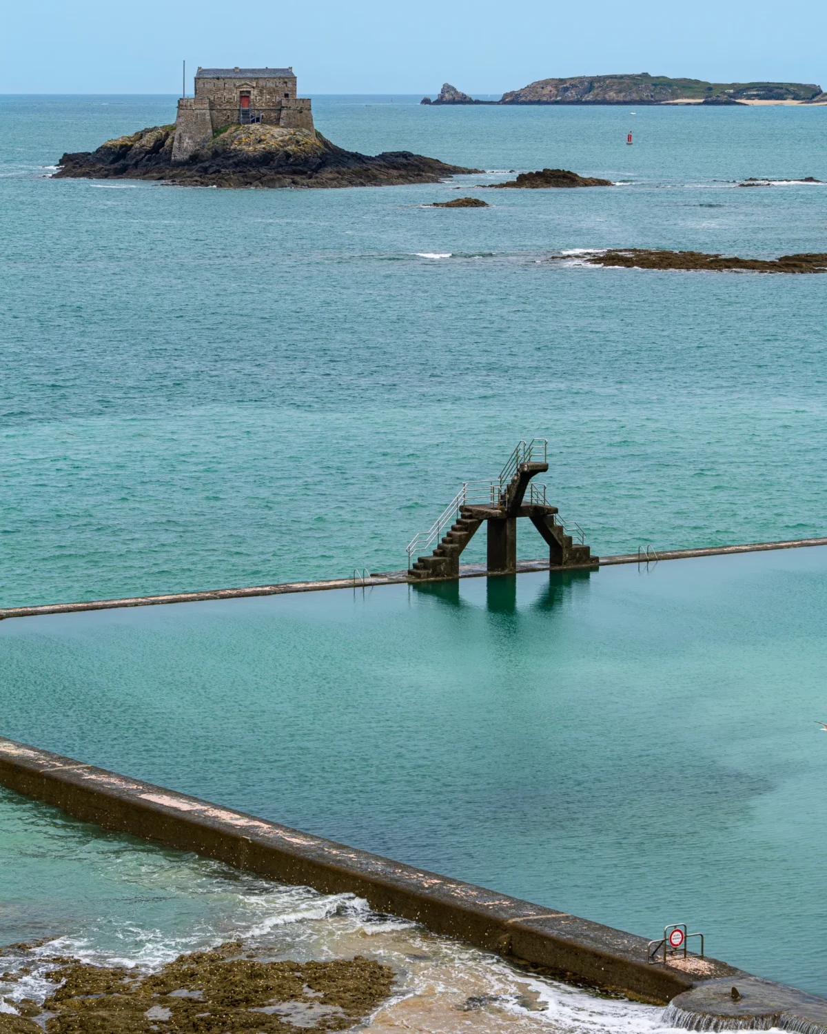 Laurent · 2160 x 2700 Cette photographie met en scène un **portique métallique rouillé** partiellement immergé en mer, sujet principal. La **composition** oppose cet élément industriel à un **paysage naturel** avec une île rocheuse à l’arrière-plan.Le **cadrage** est large, incluant une étendue d’eau turquoise et des rochers. La **lumière** semble naturelle, avec des reflets sur l’eau, créant une ambiance claire mais contrastée. Les **couleurs dominantes** sont les bleus de l’eau, le gris-vert des rochers et le rouille du métal.Le **style** est documentaire et réaliste, évoquant une **ambiance mélancolique et mystérieuse**.