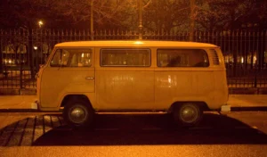 Franck T. · 20/12/2025 · 1400 x 819 Cette photographie met en scène un vieux **minibus Volkswagen** jaune, sujet principal. Le **cadrage** est serré, centré sur le véhicule, avec un arrière-plan flou composé d’une clôture et d’arbres.La **lumière**, tamisée et chaude, crée une ambiance nocturne ou crépusculaire, soulignant les contours du véhicule. Les **couleurs dominantes** sont des tons jaunes et ors, adoucis par des teintes sombres en arrière-plan.Le style évoque une **nostalgie industrielle**, renforcée par l’éclairage artificiel qui donne une touche rétro et mélancolique à la scène.