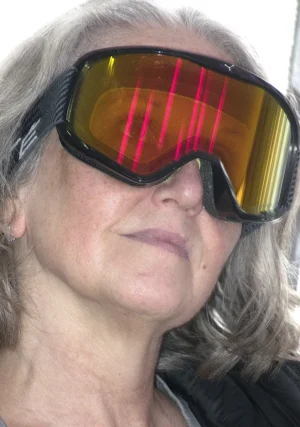 Franck T. · 06/12/2025 · 843 x 1200 Cette photographie montre une femme comme sujet principal, portant des lunettes de protection aux verres teintés orange et striés de rouge. Le cadrage est serré sur son visage, mettant l'accent sur ses yeux et ses lunettes. La lumière semble naturelle, bien que les verres colorés altèrent les teintes perçues.Les couleurs dominantes sont les tons chauds (orange, rouge) des verres, contrastant avec les nuances naturelles de sa peau et ses cheveux gris. Le style est simple et direct, sans mise en scène particulière. L'ambiance est à la fois mystérieuse et humoristique, due aux lunettes qui donnent un aspect futuriste ou protecteur.
