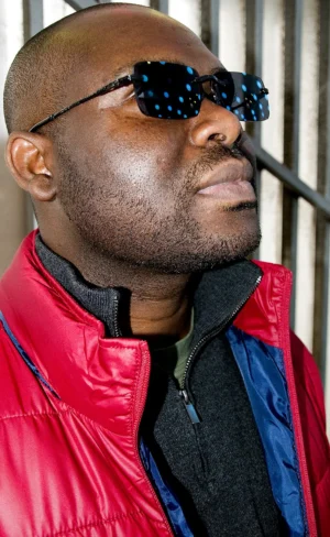 Franck T. · 06/12/2025 · 738 x 1200 Cette photographie met en scène un homme comme sujet principal, vêtu d'une veste rouge et bleue. Il porte des lunettes futuristes aux reflets bleutés et semble poser avec assurance.Le cadrage est serré, centré sur son visage et sa partie supérieure du corps. La lumière est douce mais contrastée, mettant en valeur ses traits et créant des ombres marquées sous les yeux et sur le menton.Les couleurs dominantes sont le rouge vif de sa veste et les tons bleus des lunettes. Le style est à la fois urbain et légèrement rétro-futuriste, évoquant une ambiance moderne et dynamique.
