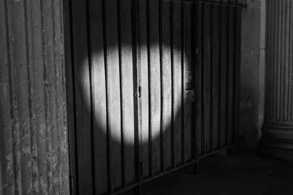 Claude · 5645 x 3763 Cette photographie met en scène un **sujet abstrait et symbolique**, où une lumière circulaire traverse des barreaux, évoquant une silhouette de cœur.La **composition** est épurée, centrée sur ce motif lumineux. Le **cadrage** est serré, isolant les barreaux et la lumière.La **lumière** est douce mais contrastée, créant une ambiance mystérieuse et presque mélancolique. Les **couleurs dominantes** sont les tons de gris et noir, renforçant l’aspect dramatique.Le **style** est minimaliste et poétique, évoquant une **ambiance onirique et introspective**, entre ombre et lumière.