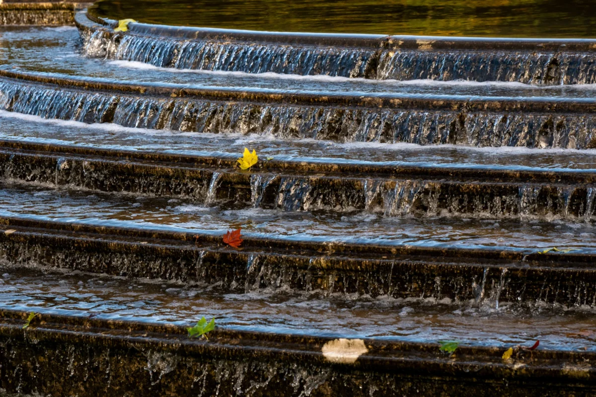Jean-Marc · 05/10/2025 · 5285 x 3523 Cette photographie met en scène des **marches d’un escalier en pierre** partiellement submergées par l’eau, formant une cascade naturelle. Le **sujet principal** est l’eau qui s’écoule, avec des **feuilles et débris** flottants.La **composition** est dynamique, avec des lignes horizontales et verticales créant un jeu de perspectives. Le **cadrage** serré isole les détails des marches et de l’eau.La **lumière** semble naturelle, tamisée, apportant une ambiance douce et mystérieuse. Les **couleurs dominantes** sont les tons bleus de l’eau et les teintes terreuses des pierres, rehaussées par les reflets dorés et les touches de vert/rouge des feuilles.Le **style** est réaliste et poétique, évoquant une **ambiance calme et contemplative**.