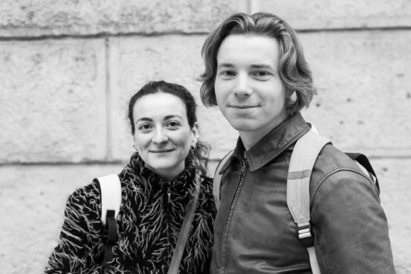 Claude · 5582 x 3721 Cette photographie en noir et blanc montre deux personnes posant côte à côte. La femme, au premier plan légèrement flou, porte un pull à motifs et un collier, tandis que l’homme, plus net, arbore une veste et un sac à dos.La composition est simple et symétrique, avec un cadrage serré sur leurs visages et épaules. La lumière douce et naturelle met en valeur leurs traits sans créer d’ombres marquées. L’ambiance est naturelle et chaleureuse, évoquant une complicité amicale ou familiale. Le style est épuré et intemporel, renforcé par le traitement monochrome.