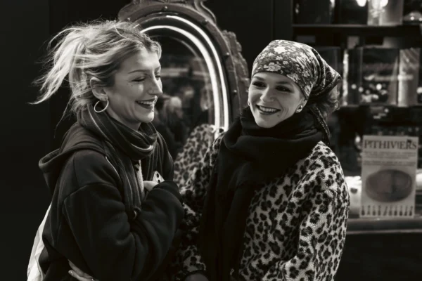 Claude · 6000 x 4000 Cette photographie met en scène deux femmes souriantes, posant côte à côte devant un miroir. Le sujet principal est leur complicité et leur expression joyeuse.La composition est symétrique, avec un cadrage serré sur les visages et les épaules. La lumière est douce et uniforme, créant des contrastes modérés. Les couleurs dominantes sont les tons de gris et noir, typiques d'un style noir et blanc, renforçant une ambiance intemporelle et élégante. L'atmosphère est chaleureuse et conviviale, évoquant une touche de modernité et de simplicité.