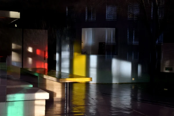 Vincent · 17/01/2026 · 5200 x 3466 Cette photographie capture une scène nocturne urbaine minimaliste. Le sujet principal semble être une structure architecturale moderne, partiellement éclairée. La composition repose sur des formes géométriques et des jeux d’ombres. Le cadrage est serré, mettant en valeur des reflets lumineux sur une surface mouillée.Les couleurs dominantes sont les teintes sombres (noir, gris) avec des éclats de rouge, vert et jaune, créant un contraste saisissant. Le style est épuré et abstrait, évoquant une ambiance mystérieuse et presque onirique. La lumière, dynamique et contrastée, accentue l’atmosphère nocturne et industrielle.