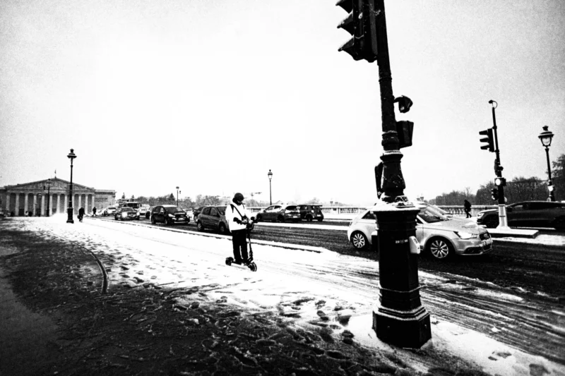Thierry · 05/01/2026 · 3840 x 2560 Cette photographie en noir et blanc capture une scène urbaine hivernale. Le sujet principal est un homme marchant seul sur un trottoir enneigé, près d’un carrefour. La composition met en valeur les éléments architecturaux classiques en arrière-plan et les véhicules stationnés.Le cadrage est serré sur le premier plan avec le lampadaire et l’homme, créant une profondeur de champ. La lumière est diffuse, typique d’un jour gris et froid. Les couleurs dominantes, bien que monochromes, jouent sur les contrastes de tons clairs et sombres.Le style est documentaire et intemporel, évoquant une ambiance mélancolique et paisible.
