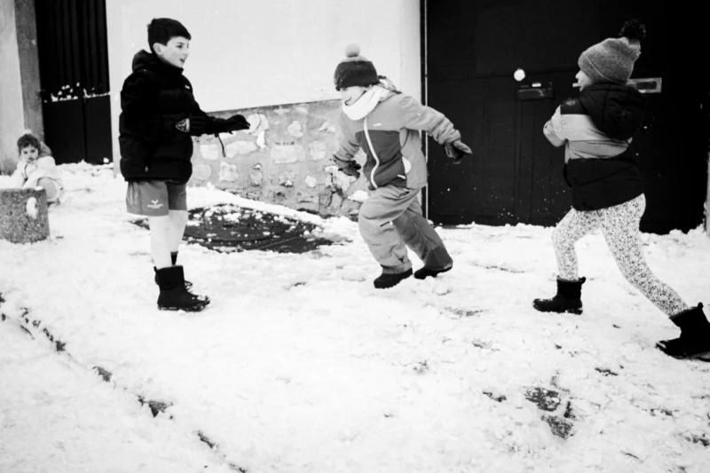 Thierry · 07/01/2026 · 3840 x 2560 Cette photographie en noir et blanc capture trois enfants en plein jeu dans la neige. Le sujet principal est leur interaction dynamique autour d’un objet, probablement un traîneau.La composition montre un cadrage serré, mettant en valeur leurs mouvements énergiques. La lumière semble naturelle, avec des contrastes marqués créant des ombres nettes. L’ambiance est joyeuse et spontanée, évoquant l’insouciance de l’enfance en hiver. Le style est documentaire, authentique, renforcé par le monochrome. Les couleurs dominantes, bien que grises, suggèrent des tons froids et lumineux, typiques d’un paysage enneigé.