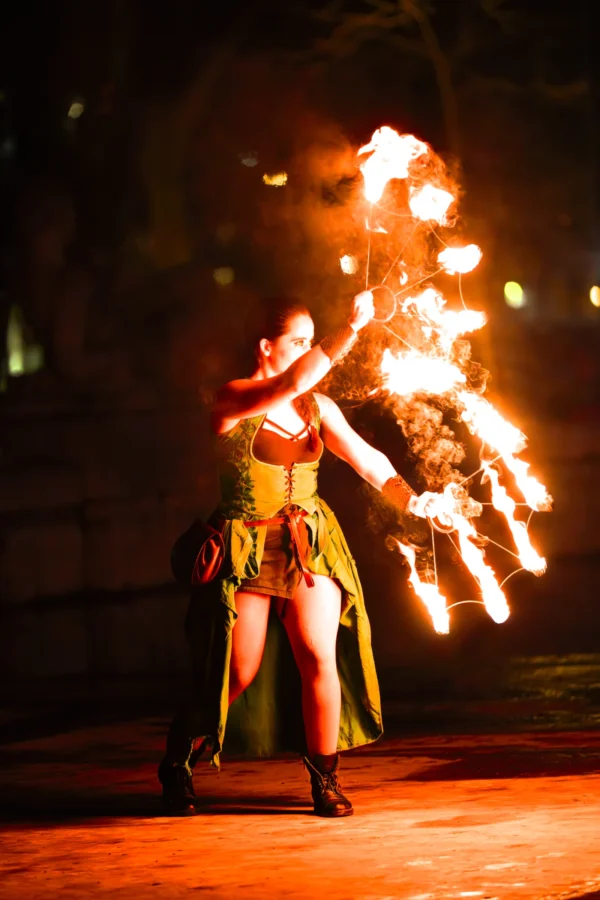Thierry · 24/01/2026 · 2560 x 3840 Cette photographie met en scène une artiste de feu comme sujet principal. Elle porte une tenue colorée, jaune et verte, avec des flammes jaillissant de ses mains.La composition est dynamique, centrée sur l'artiste en mouvement. Le cadrage est serré, mettant en valeur ses gestes et les flammes. La lumière est dramatique, avec des éclats vifs des torches contrastant avec l'obscurité ambiante.Les couleurs dominantes sont les jaunes et oranges des flammes, sur un fond sombre. Le style évoque un spectacle de rue ou un art performatif. L'ambiance est intense et captivante, mêlant énergie et mystère.