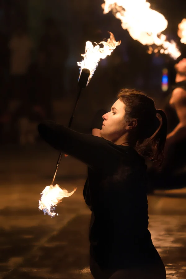 Ahmet · 24/01/2026 · 1706 x 2560 Cette photographie met en scène une personne comme sujet principal, manipulant des torches enflammées avec grâce. La composition est dynamique, centrée sur le mouvement et l'énergie. Le cadrage serré isole le sujet, mettant l'accent sur ses gestes précis.Les flammes, éclairées par une lumière vive et contrastée, dominent avec des teintes orangées et jaunes. L’ambiance est nocturne, mystérieuse et intense, renforcée par les ombres et la faible lumière environnante. Le style évoque l’art performatif et le spectacle, créant une atmosphère à la fois envoûtante et dramatique.