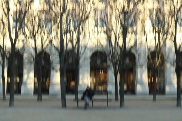 Francoise · 03/01/2026 · 5833 x 3888 Cette photographie montre un **sujet principal** flou, une personne assise sur un banc dans un parc. La **composition** est simple, avec des arbres dénudés en arrière-plan et des structures architecturales lumineuses.Le **cadrage** est large, capturant une scène paisible et légèrement estompée. La **lumière**, douce et dorée, évoque un coucher ou lever de soleil, créant une ambiance chaleureuse et apaisante. Les **couleurs dominantes** sont des tons neutres (beige, gris) adoucis par des reflets dorés.Le **style** est réaliste et légèrement flou, donnant une impression de tranquillité et de mélancolie. L’**ambiance** est calme et introspective, renforcée par la solitude du personnage.