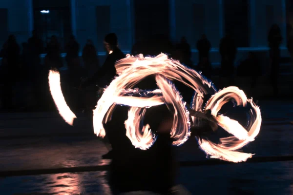 Ahmet · 24/01/2026 · 2560 x 1706 Cette photographie capture un artiste manipulant des **brûleurs de feu** (ou fire poi), sujet principal dynamique et central. La **composition** met en valeur les mouvements circulaires lumineux, créés par les sphères enflammées, formant des spirales hypnotiques.Le **cadrage** est serré, isolant l’artiste dans une ambiance nocturne. La **lumière** est contrastée : éclats vifs des flammes sur un fond sombre, accentuant le mouvement. Les **couleurs dominantes** sont les teintes chaudes des feux (oranges, jaunes) sur un arrière-plan bleuté-noir.Le style est **artistique et énergique**, évoquant une ambiance **spectaculaire et mystique**, typique des performances de feu en extérieur.