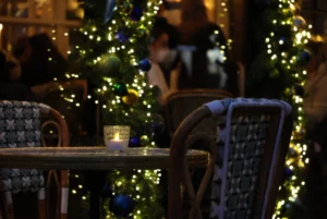 Laurence · 20/12/2025 · 3472 x 2320 Cette photographie met en scène une ambiance festive et intimiste. Le sujet principal semble être une table festive décorée pour les fêtes, avec des bougies et des éléments décoratifs.La composition montre un cadrage serré sur un espace restreint, avec une table et des chaises en premier plan. L'arrière-plan est flou, mettant en valeur les lumières scintillantes d'un sapin décoré.Les couleurs dominantes sont les teintes chaudes des lumières (jaunes, blanches) et les verts du sapin. La lumière crée une ambiance chaleureuse et conviviale, typique des célébrations hivernales. Le style est réaliste et naturel, renforçant l'atmosphère cosy et réconfortante.