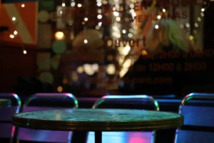 Laurence · 20/12/2025 · 3472 x 2320 Cette photographie montre un intérieur de bar ou de restaurant peu éclairé. Le sujet principal est une table ronde vide avec des chaises en métal autour, légèrement floues. La composition met en avant un cadrage serré sur l’avant-plan, avec une profondeur de champ réduite, créant un effet bokeh dans l’arrière-plan.Les lumières colorées (bleues, violettes) et les néons ajoutent une ambiance festive et tamisée. Les couleurs dominantes sont les tons sombres et les éclats lumineux colorés. Le style est moderne et urbain, évoquant une ambiance nocturne et détendue.