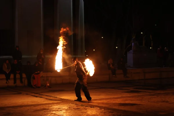 Laurence · 2719 x 1813 Cette photographie capture un artiste manipulant des boules de feu lors d'une performance nocturne. Le sujet principal est l'artiste en mouvement, au centre de l'image, avec des flammes vives en rotation.La composition est dynamique, avec un cadrage serré sur l'artiste et ses boules de feu. Les lumières chaudes dominent, créant un contraste saisissant avec l'obscurité ambiante. Les couleurs principales sont les tons orangés et jaunes des flammes, sur un fond sombre.L'ambiance est spectaculaire et intense, évoquant une scène de spectacle vivant et captivante. Le style est réaliste et spontané, mettant en valeur l'action et l'énergie du moment.