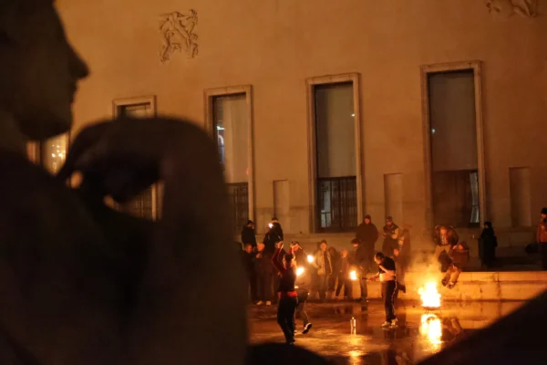Laurence · 3472 x 2315 Cette photographie capture une scène nocturne de protestation ou de rassemblement. Le sujet principal semble être un groupe de personnes autour d’un feu ou d’une source lumineuse intense, créant une ambiance dramatique.La composition montre un cadrage serré sur le premier plan, avec une silhouette floue en avant, tandis que le groupe est en arrière-plan. Les lumières chaudes dominent, avec des teintes orangées et des ombres marquées, renforçant l’atmosphère tendue et mystérieuse. Le style est documentaire et spontané, évoquant une ambiance de tension et d’émotion collective.