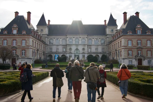 Paul C. · 17/01/2026 · 5948 x 3962 Cette photographie montre un groupe de personnes marchant vers un imposant château à l'architecture classique. Le sujet principal est ce château, avec ses toits en ardoise et ses nombreuses fenêtres symétriques.La composition est axée sur la perspective, avec les visiteurs au premier plan et le château en arrière-plan. Le cadrage est serré sur les personnes, mais inclut suffisamment d'éléments architecturaux pour donner une idée de l'ensemble.La lumière est douce, avec un éclairage naturel qui crée des ombres légères. Les couleurs dominantes sont les tons neutres (beige, gris) du château, contrastant avec les vêtements colorés des visiteurs. L'ambiance est calme et majestueuse, évoquant l'histoire et la grandeur.