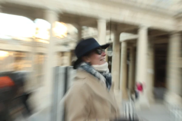 Francoise · 03/01/2026 · 6000 x 4000 Cette photographie présente un sujet principal flou, une personne en mouvement portant un chapeau et une veste beige. La composition est dynamique, avec un cadrage serré et une légère profondeur de champ. L'arrière-plan, légèrement déformé, montre des colonnes et des lumières de rue, suggérant un lieu urbain.La lumière est douce mais diffuse, créant une ambiance tamisée. Les couleurs dominantes sont des tons neutres (beige, gris) avec des éclats de lumière chaude. Le style est réaliste et spontané, évoquant une impression de vie quotidienne et de mouvement rapide. L'ambiance est à la fois urbaine et intimiste.