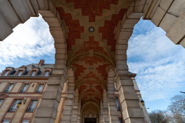 Marc · 17/01/2026 · 7008 x 4672 Cette photographie met en scène un **arc architectural** en pierre, probablement une porte monumentale ou un passage voûté. Le **sujet principal** est l’arche ornée de briques rouges et de motifs géométriques.La **composition** joue sur la perspective, avec un **cadrage serré** qui accentue la profondeur et la symétrie. La **lumière**, naturelle et contrastée, éclaire l’arche tout en créant des ombres marquées. Les **couleurs dominantes** sont les tons beiges des pierres, les rouges des briques et le bleu du ciel visible en arrière-plan.Le **style** évoque l’architecture classique ou médiévale, tandis que l’**ambiance** est à la fois majestueuse et mystérieuse, renforcée par les jeux d’ombre et de lumière.