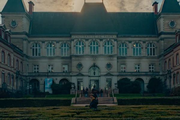 Don · 4549 x 3033 Cette photographie met en scène un **imposant bâtiment historique** aux allures de château ou d’institution ancienne, avec une architecture classique et des arcs en bas-relief.**Composition** : Symétrique, centrée sur une cour avec une statue au premier plan.
**Cadrage** : Plan moyen, incluant un groupe de personnes en discussion devant l’édifice.
**Lumière** : Naturelle, douce et tamisée, avec des ombres marquées, suggérant un coucher de soleil.
**Couleurs** : Dominées par des tons **beige, gris et verts** adoucis, avec des teintes chaudes en arrière-plan.
**Style** : Cinématographique, presque onirique.
**Ambiance** : Mystérieuse et solennelle, évoquant une atmosphère à la fois historique et légèrement inquiétante.