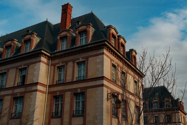 Don · 6346 x 4231 Cette photographie met en scène un immeuble de style architectural classique, probablement du XIXe siècle, avec des détails comme des mansardes, des fenêtres alignées et des briques apparentes.La composition est verticale, centrée sur l’immeuble avec un cadrage serré. La lumière, douce et légèrement dorée, suggère un moment en fin de journée. Les couleurs dominantes sont des tons beiges, bruns et gris, adoucis par des touches de rouge sur les toits.L’ambiance est à la fois élégante et nostalgique, évoquant un quartier historique et paisible.