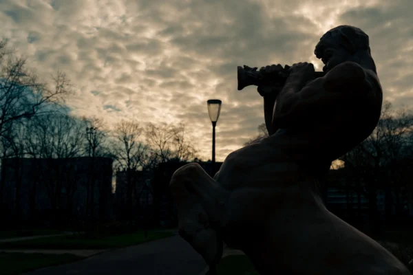 Don · 6028 x 4019 Cette photographie met en scène une statue en silhouette, sujet principal, représentant une personne filmant avec une caméra ancienne. La composition est simple et épurée, avec un cadrage serré sur la statue, isolée sur un fond de ciel nuageux.La lumière, tamisée et douce, crée un contraste entre les ombres et les zones éclairées, accentuant le côté dramatique. Les couleurs dominantes sont les teintes sombres et grises, avec des touches de bleu et de noir dans le ciel.Le style est réaliste et photographique, évoquant une ambiance mélancolique et contemplative.