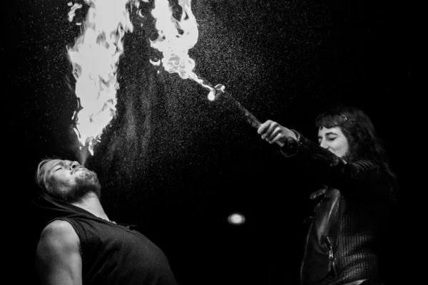 Don · 24/01/2026 · 3146 x 2097 Cette photographie en noir et blanc met en scène deux personnes pratiquant un numéro de feu. Le sujet principal est l’un d’eux tenant une torche enflammée près du visage de l’autre, allongé.La composition est dynamique, avec un cadrage serré qui isole les deux individus. La lumière est dramatique, centrée sur les flammes, créant des contrastes forts et des ombres marquées. L’ambiance est intense et théâtrale, évoquant tension et spectacle. Le style est artistique et expressif, renforcé par le monochrome.