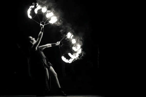 Don · 24/01/2026 · 3537 x 2358 Cette photographie met en scène une artiste manipulant des feux enflammés, probablement lors d’un spectacle de feu. Le sujet principal est dynamique, en mouvement, avec des flammes formant des cercles lumineux autour d’elle.La composition est centrée, avec un cadrage serré qui isole le sujet. La lumière est dramatique, contrastée, avec des flammes vives sur un fond noir. Les couleurs dominantes sont les teintes chaudes des feux (blancs, jaunes, oranges) sur un arrière-plan monochrome sombre.Le style est artistique et théâtral, évoquant une ambiance mystique et captivante, typique des performances de feu.