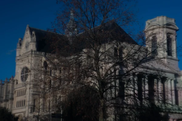 Alice · 03/01/2026 · 7008 x 4672 Cette photographie met en scène un bâtiment gothique, probablement une cathédrale ou une église, avec des éléments architecturaux caractéristiques comme des arcs brisés et des tours.La composition montre l'édifice partiellement caché par des arbres sans feuilles. Le cadrage est serré, centré sur la structure, avec un ciel bleu profond en arrière-plan.La lumière semble naturelle, probablement en fin de journée, créant des contrastes marqués. Les couleurs dominantes sont les tons gris-beige du bâtiment et le bleu du ciel. L’ambiance est à la fois mystérieuse et solennelle, renforcée par les ombres et la silhouette des arbres.