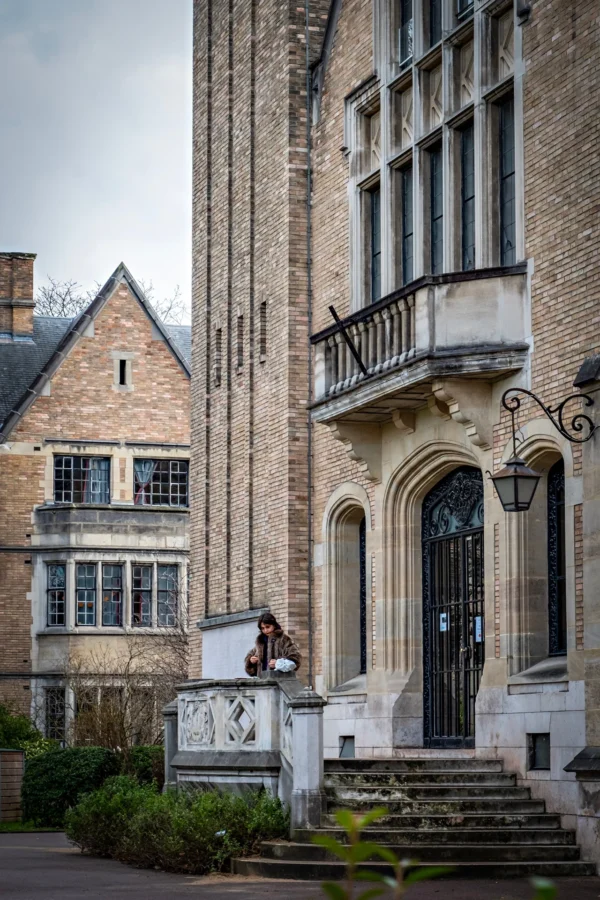 AnJo · 17/01/2026 · 1280 x 1920 Cette photographie met en scène une façade de bâtiment historique, probablement une vieille demeure ou un édifice académique. Le sujet principal est l'entrée majestueuse avec ses détails architecturaux : porte en bois, balustrade en fer forgé et escalier en pierre.La composition est symétrique, avec un cadrage serré sur l'entrée, encadrée par des murs en pierre. La lumière, douce et naturelle, semble tamisée, créant des ombres légères. Les couleurs dominantes sont les tons gris-beige des pierres, rehaussés par des touches de vert et de noir.L'ambiance est sobre et élégante, évoquant un style classique et intemporel.