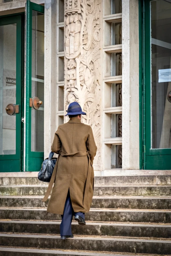 AnJo · 17/01/2026 · 1280 x 1920 Cette photographie met en scène un homme vêtu d’un uniforme militaire d’époque, vu de dos, portant un sac et un casque. La composition est centrée sur ce personnage, encadré par une porte et une fenêtre ornées de motifs sculptés.Le cadrage est serré, mettant en valeur les détails de l’uniforme et de l’architecture. La lumière, naturelle et douce, éclaire le sujet par la gauche, créant des contrastes subtils. Les couleurs dominantes sont les tons beiges et verts, avec des détails en gris et blanc.Le style évoque une ambiance historique et mélancolique, renforcée par les éléments architecturaux classiques.