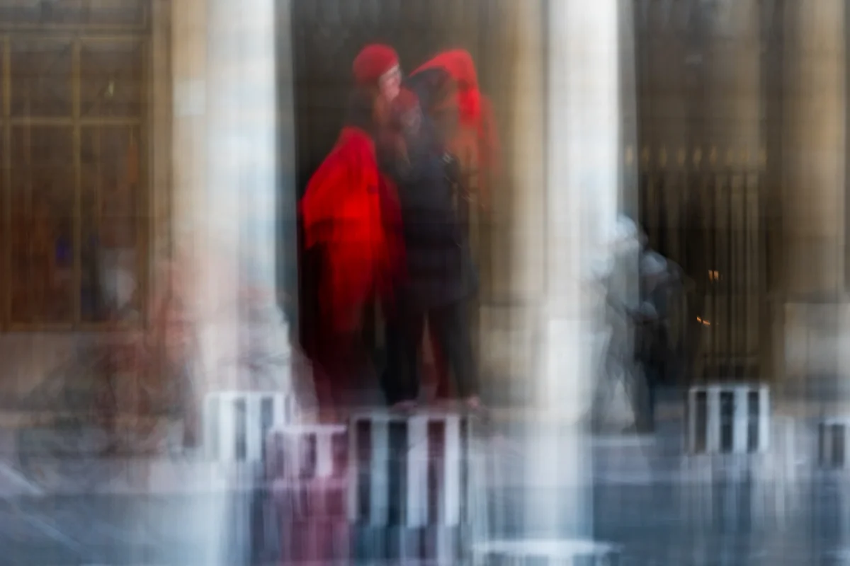 Jean-Marc · 03/01/2026 · 4935 x 3290 Cette photographie met en scène un couple flou en mouvement, vêtu de manteaux sombres et d’un élément rouge vif, probablement un manteau ou un accessoire. La composition repose sur un cadrage serré et une perspective basse, accentuant la verticalité des colonnes et des barrières en métal.La lumière est tamisée, créant une ambiance mystérieuse et onirique. Les couleurs dominantes sont les tons froids grisâtres, contrastant avec le rouge éclatant, qui attire l’attention. Le style est artistique et abstrait, évoquant une impression de vitesse et de flou artistique. L’ambiance est à la fois urbaine et poétique, presque mélancolique.