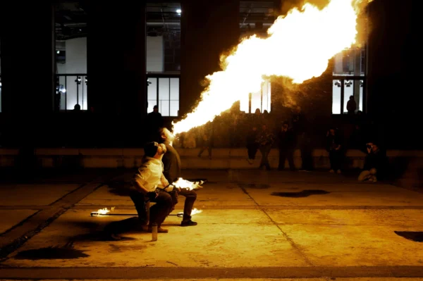 Cyrille · 24/01/2026 · 2026 x 1347 Cette photographie capture un artiste manipulant une torche à feu, projetant une grande flamme orange et jaune. Le sujet principal est donc le performeur et son élément pyrotechnique.La composition est dynamique, centrée sur l'action. Le cadrage est serré, mettant en valeur la scène nocturne. Les couleurs dominantes sont les tons chauds des flammes, contrastant avec l'obscurité ambiante. La lumière est vive et contrastée, créant une ambiance dramatique et intense. Le style semble documentaire ou artistique, capturant un moment spectaculaire et captivant.