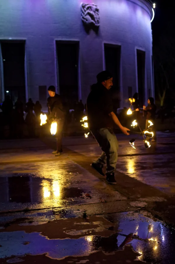 Cyrille · 24/01/2026 · 1347 x 2026 Cette photographie capture un **artiste de feu** en action, manipulant des torches enflammées lors d’un spectacle nocturne. Le **sujet principal** est dynamique, au premier plan, avec un mouvement fluide.La **composition** est équilibrée, mettant en valeur le performer devant un **fond architectural** (bâtiment éclairé). Le **cadrage** est serré, accentuant l’intensité de la scène.Les **lumières** sont contrastées : clarté des flammes et ombres profondes. Les **couleurs dominantes** sont les teintes chaudes (oranges, jaunes) des torches, contrastant avec le bleu nuit de l’arrière-plan.Le **style** est artistique et théâtral, créant une **ambiance** envoûtante, presque mystique, mêlant énergie et poésie.