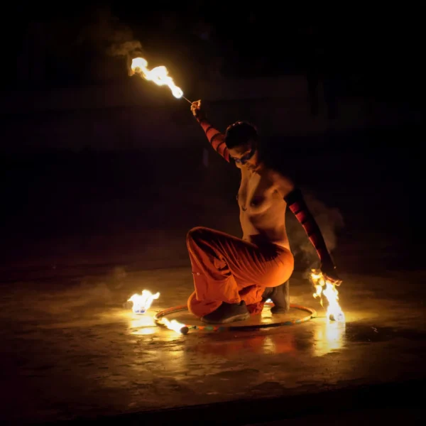 Cyrille · 24/01/2026 · 2026 x 2026 Cette photographie met en scène un artiste manipulant des torches enflammées, sujet principal dynamique et central. La composition est épurée, avec un cadrage serré qui isole le performer sur fond sombre.Les flammes, éclairant son corps, créent un jeu de lumière dramatique. Les couleurs dominantes sont les tons chauds (oranges, jaunes) des feux contrastant avec les ombres nocturnes.Le style évoque l’art traditionnel ou le spectacle de rue, tandis que l’ambiance est intense, presque mystique, renforcée par la nuit et les éclats lumineux.