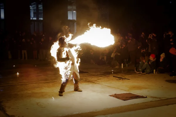 Cyrille · 24/01/2026 · 2026 x 1347 Cette photographie capture un artiste de feu en action. Le sujet principal est un performer manipulant une torche enflammée, vêtu de vêtements clairs.La composition montre une scène nocturne avec un cadrage serré sur l'artiste, mettant en valeur son mouvement dynamique. L'arrière-plan est flou, avec une foule en spectateurs.La lumière est vive et contrastée, avec des teintes chaudes dominées par les flammes jaunes et blanches. L'ambiance est spectaculaire et intense, évoquant une performance artistique et énergique.