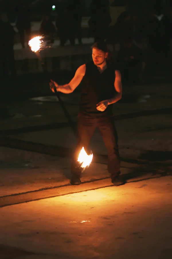 Fabienne · 24/01/2026 · 2150 x 3225 Cette photographie montre un artiste de rue manipulant des objets enflammés, probablement des torches ou des bâtons à feu. Le sujet principal est centré, avec un cadrage serré mettant en valeur son action dynamique.La lumière est dramatique, avec des flammes vives contrastant sur un fond sombre. Les couleurs dominantes sont les teintes chaudes des flammes (oranges et jaunes) et les tons sombres de la nuit. Le style est réaliste et spontané, capturant un moment intense. L’ambiance est mystérieuse et captivante, évoquant le spectacle et la maîtrise du feu.