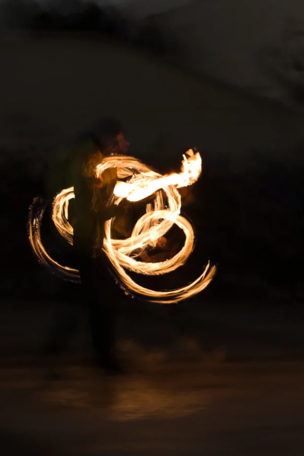 Fabienne · 24/01/2026 · 1706 x 2559 Cette photographie capture un artiste en train de manipuler des torches enflammées, créant des motifs lumineux en mouvement. Le sujet principal est ces spirales de feu, dynamiques et fluides. La composition est épurée, centrée sur la lumière et le mouvement. Le cadrage est serré, isolant presque totalement le sujet dans l’obscurité.Les couleurs dominantes sont les teintes chaudes des flammes (jaunes, oranges) contrastant avec le noir ambiant. Le style est artistique et expressif, évoquant une ambiance mystique et hypnotique, typique des spectacles de feu. L’éclairage dramatique accentue le côté spectaculaire et presque magique de la scène.
